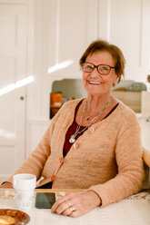 Porträt einer lächelnden älteren Frau im Ruhestand, die am Tisch im Pflegeheim sitzt - MASF12573