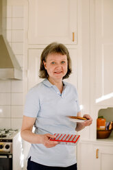 Porträt einer lächelnden reifen Mitarbeiterin des Gesundheitswesens, die in einer Küche Medikamente und einen Teller hält - MASF12574