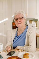 Porträt einer älteren Frau im Ruhestand, die mit ihrem Smartphone am Tisch eines Pflegeheims sitzt - MASF12576