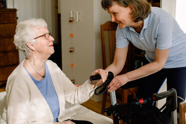 Eine lächelnde Pflegekraft betrachtet eine ältere Frau, die mit einem Rollator im Zimmer eines Pflegeheims sitzt - MASF12585