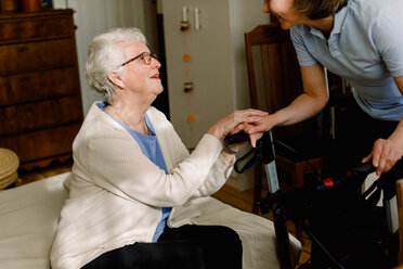 Lächelnde ältere Frau, die die Hände eines weiblichen Pflegepersonals im Schlafzimmer eines Pflegeheims hält - MASF12587