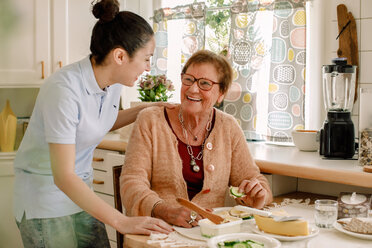 Fröhliche ältere Frau im Gespräch mit einer Pflegerin in der Küche eines Pflegeheims - MASF12590