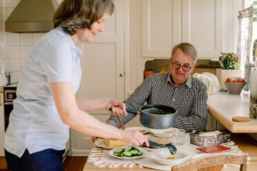 Side view of female caregiver is serving meal at table for retired senior man sitting in nursing home - MASF12595