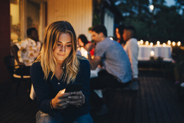 Young woman using smart phone while friends in background during dinner party - MASF12605