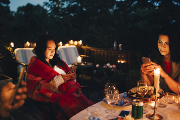 Female friends using mobile phones at table during dining party - MASF12607