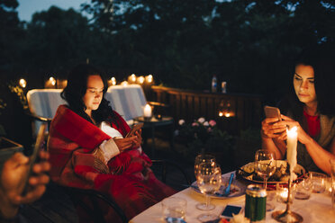 Freundinnen benutzen Mobiltelefone am Tisch während einer Dinnerparty - MASF12607