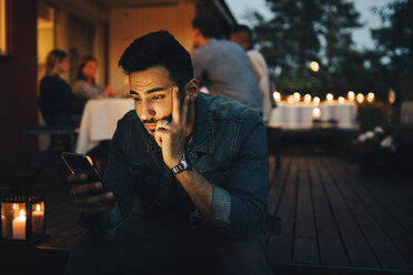 Man using mobile phone while friends in background during dinner party - MASF12613