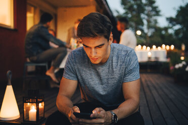 Young man using smart phone while friends in background during dinner party - MASF12616