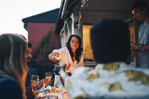 Junge Frau serviert einem Freund am Tisch während einer Dinnerparty ein Getränk - MASF12628