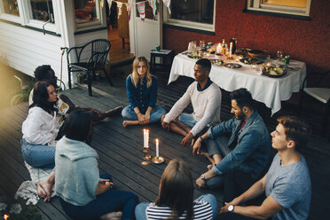 High angle view of male and female friends sitting with eyes closed around lit candles in balcony during group therapy s - MASF12639