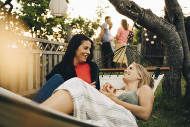 Happy female friends relaxing on hammock at yard during sunset - MASF12646