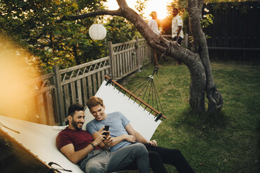 Hoher Blickwinkel von lächelnden Freunden, die ihr Smartphone benutzen, während sie sich in der Hängematte im Garten ausruhen - MASF12652