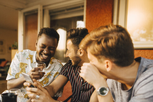 Fröhliche männliche Freunde benutzen ein Smartphone, während sie sich auf einer Dinnerparty amüsieren - MASF12656