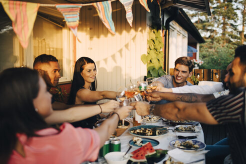 Lächelnde Freunde stoßen mit Getränken am Esstisch in einer Dinnerparty an - MASF12666