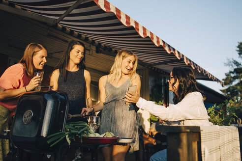 Lächelnde Frau zeigt Freunden beim Grillen ihr Handy - MASF12674