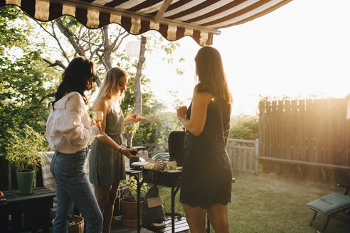 Weibliche Freunde unterhalten sich bei der Zubereitung von Speisen auf einem Grill in einer Dinnerparty - MASF12679