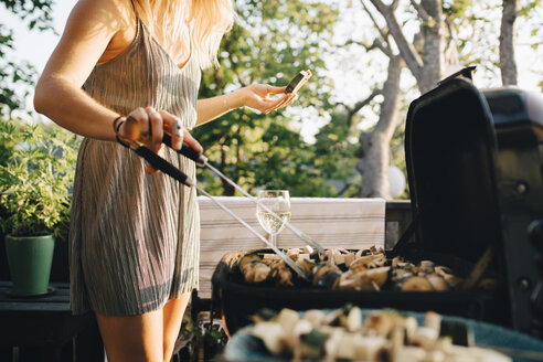 Mittelteil einer Frau, die Gemüse auf dem Grill grillt und Wassermelone isst - MASF12683