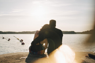 Rückansicht eines romantischen Paares, das im Sommer auf einem Steg am See sitzt - MASF12699