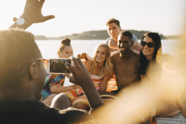 Mann fotografiert im Sommer fröhliche Freunde mit dem Handy am Bootssteg - MASF12701