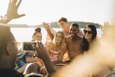 Man photographing happy friends on smart phone at jetty in summer - MASF12705