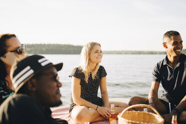 Fröhliche multiethnische Freunde unterhalten sich im Sommer auf einem Steg am See - MASF12710