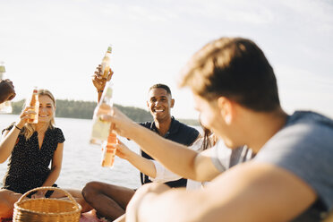 Freunde genießen Getränke, während sie auf dem Steg gegen den Himmel im Sommer sitzen - MASF12711