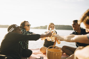 Freunde stoßen mit Flaschen an, während sie im Sommer auf dem Steg gegen den Himmel sitzen - MASF12713