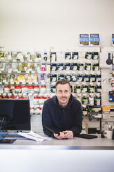 Lächelnder männlicher Verkäufer, der bei der Arbeit in einem Elektronikgeschäft wegschaut - MASF12718
