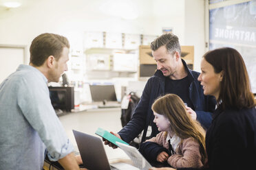 Älterer Mann sieht sich ein Paket an, während er mit seiner Familie in einem Elektronikgeschäft steht - MASF12744