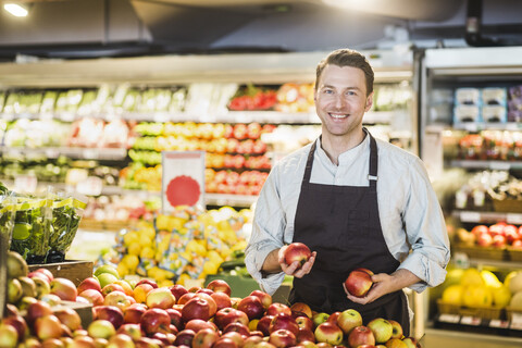 Porträt eines lächelnden reifen Besitzers, der an einem Apfelstand in einem Lebensmittelgeschäft steht, lizenzfreies Stockfoto
