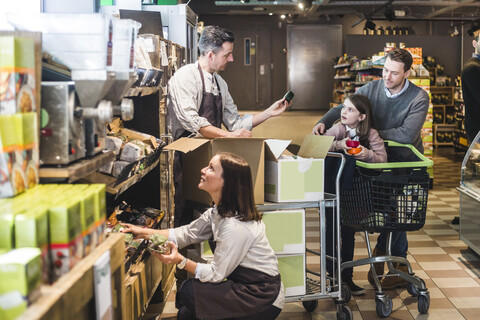 Verkäufer, der Kunden bedient, während die Verkäuferin das Regal im Supermarkt ordnet, lizenzfreies Stockfoto
