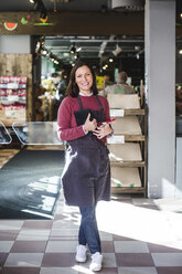 Ganzes Porträt einer lächelnden reifen Verkäuferin mit Schürze, die in einem Geschäft steht - MASF12781