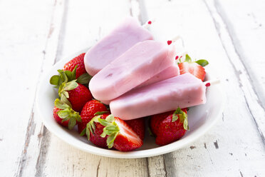 Hausgemachte Erdbeer-Joghurt-Eislutscher mit frischen Erdbeeren in einer Schale auf weißem Holz - LVF08071