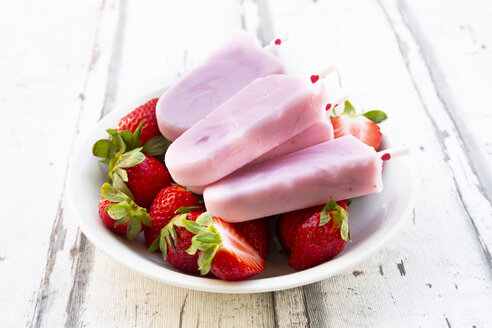 Hausgemachte Erdbeer-Joghurt-Eislutscher mit frischen Erdbeeren in einer Schale auf weißem Holz - LVF08071