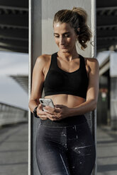 Sporty woman with headphones standing on bridge, listening music, using smartphone - ERRF01465