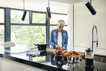 Ältere Frau steht in der Küche und schneidet Erdbeeren - ZEDF02319