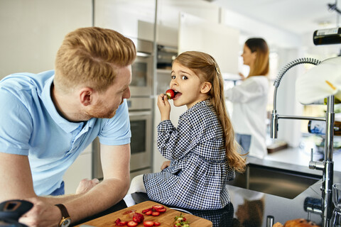 Glückliche Familie isst frische Erdbeeren in einer modernen Küche, lizenzfreies Stockfoto