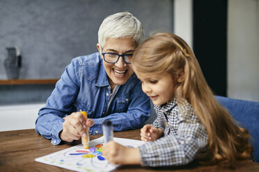 Grandmother and granddaughter sitting at table, painting colouring book - ZEDF02353