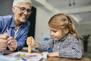 Grandmother and granddaughter sitting at table, painting colouring book - ZEDF02356