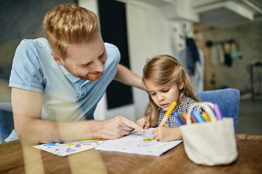 Father and daughter sitting at table, painting colouring book - ZEDF02358