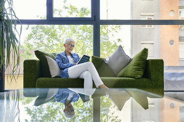 Senior woman sitting on couch, reading a book - ZEDF02363