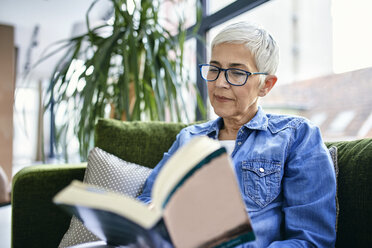 Senior woman sitting on couch, reading a book - ZEDF02364