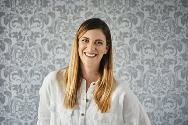 Portrait of a happy, blond woman in front of patterned wallpaper - ZEDF02371