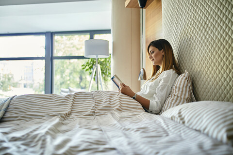 Frau sitzt im Bett und liest ein Buch, lizenzfreies Stockfoto