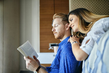 Affectionate couple reading book together in bedroom - ZEDF02400