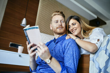 Affectionate couple reading book together in bedroom - ZEDF02402