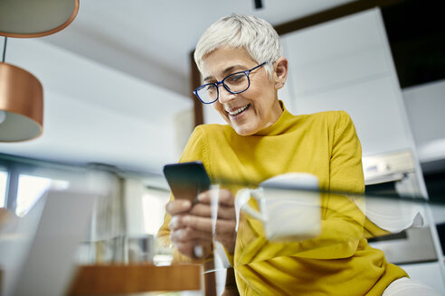 Ältere Frau trinkt Kaffee und überprüft Textnachrichten auf ihrem Smartphone - ZEDF02406