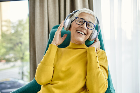 Ältere Frau sitzt im Sessel und hört Musik mit Kopfhörern, lizenzfreies Stockfoto
