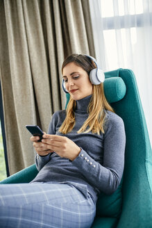 Frau im Sessel sitzend, mit Kopfhörern Musik hörend, mit Smartphone - ZEDF02415