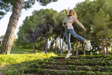 Young redheaded woman jumping on steps in a park - AFVF03170
